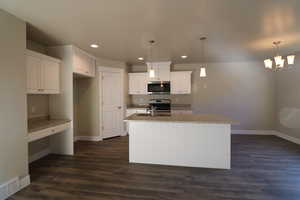 Kitchen with pendant lighting, stainless steel microwave, white cabinetry, and an island with sink