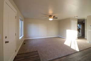 Empty room featuring visible vents, dark wood-type flooring, ceiling fan, baseboards, and stairs