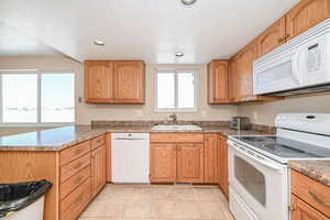 Kitchen with a textured ceiling, recessed lighting, a peninsula, white appliances, and a sink