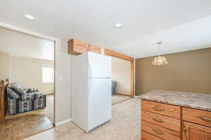 Kitchen featuring a textured ceiling, a chandelier, baseboards, hanging light fixtures, and freestanding refrigerator