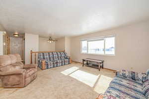 Living area with a textured ceiling, ceiling fan, and light carpet