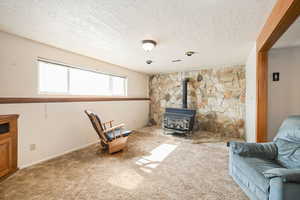 Living area featuring carpet floors, a wood stove, visible vents, and a textured ceiling