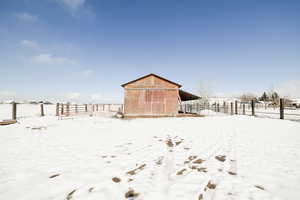 Snow covered structure featuring an outbuilding and fence