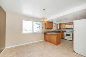 Kitchen with white appliances, brown cabinets, a peninsula, light countertops, and a sink