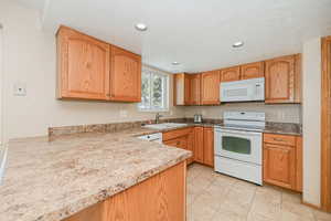 Kitchen with a textured ceiling, recessed lighting, white appliances, a sink, and light countertops