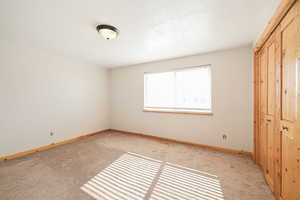 Unfurnished bedroom with a textured ceiling, light carpet, visible vents, baseboards, and a closet