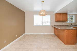 Kitchen featuring hanging light fixtures, baseboards, brown cabinets, and a sink