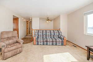 Living room with ceiling fan, a textured ceiling, light colored carpet, visible vents, and baseboards