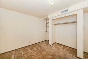 Unfurnished bedroom featuring light carpet, baseboards, visible vents, a textured ceiling, and a closet