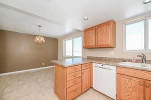 Kitchen with a peninsula, a sink, light countertops, dishwasher, and decorative light fixtures