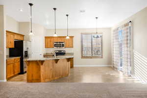 Kitchen featuring visible vents, a center island with sink, appliances with stainless steel finishes, and light colored carpet