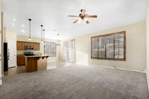 Kitchen with light carpet, an island with sink, open floor plan, hanging light fixtures, and stainless steel appliances