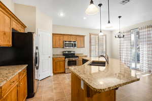 Kitchen featuring a center island with sink, visible vents, appliances with stainless steel finishes, pendant lighting, and a sink