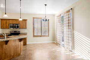 Kitchen featuring a breakfast bar, a sink, appliances with stainless steel finishes, brown cabinets, and decorative light fixtures