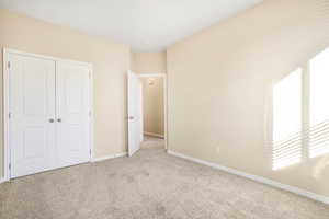 Unfurnished bedroom with light carpet, a closet, and baseboards