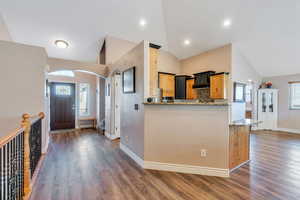 Kitchen with arched walkways, a peninsula, dark wood-style floors, and light stone countertops