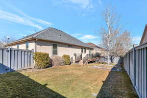 Rear view of property with a shingled roof, a fenced backyard, a deck, a yard, and stucco siding