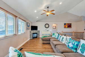 Living area featuring light wood finished floors, visible vents, arched walkways, vaulted ceiling, and a fireplace