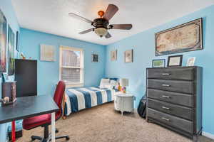 Carpeted bedroom with a ceiling fan, a textured ceiling, and baseboards