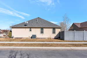 View of property exterior featuring a shingled roof, fence, cooling unit, and stucco siding