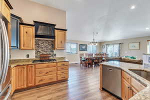 Kitchen featuring tasteful backsplash, hanging light fixtures, appliances with stainless steel finishes, open floor plan, and premium range hood