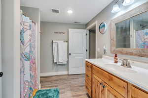 Bathroom with a textured ceiling, visible vents, wood finished floors, and vanity