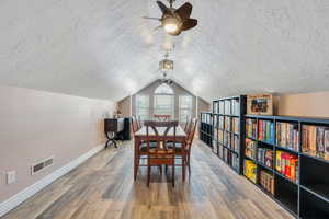 Dining space featuring baseboards, visible vents, lofted ceiling, wood finished floors, and a textured ceiling