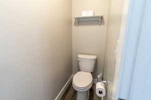 Bathroom featuring wood finished floors, toilet, and baseboards