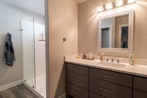 Full bath featuring a shower stall, baseboards, wood finished floors, and vanity