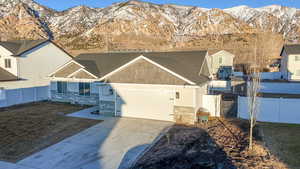 View of front of house featuring stone siding, a mountain view, concrete driveway, and fence