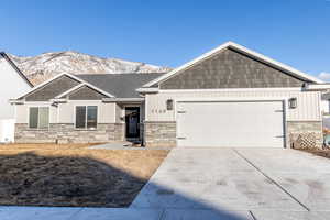 View of front of home with an attached garage, a mountain view, driveway, stone siding, and board and batten siding