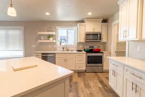 Kitchen featuring light wood finished floors, stainless steel appliances, hanging light fixtures, a sink, and light stone countertops