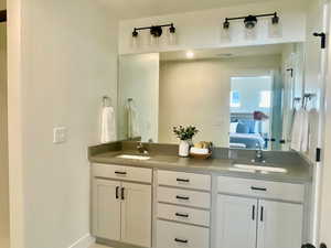 Ensuite bathroom featuring double vanity, connected bathroom, visible vents, and a sink