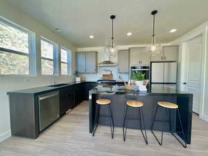 Kitchen with a sink, appliances with stainless steel finishes, gray cabinets, a center island, and dark countertops