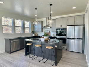 Kitchen with wall chimney exhaust hood, a kitchen island, appliances with stainless steel finishes, gray cabinetry, and a sink