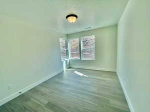 Spare room featuring light wood-style flooring, a textured ceiling, visible vents, and baseboards