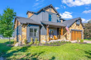 View of front of house featuring stone siding, an attached garage, covered porch, board and batten siding, and a front yard