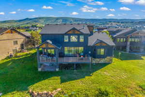 Rear view of house with a deck with mountain view, a shingled roof, a residential view, and a lawn