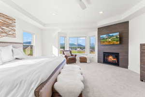 Bedroom featuring light carpet, multiple windows, a fireplace, and a raised ceiling