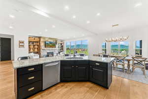 Kitchen featuring a spacious island, stainless steel dishwasher, open floor plan, a sink, and dark cabinetry