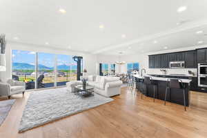 Living room with a notable chandelier, recessed lighting, a mountain view, light wood-type flooring, and beamed ceiling