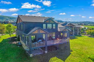 Rear view of property featuring a deck with mountain view, a shingled roof, and a yard