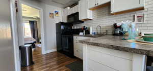 Kitchen with black appliances, dark countertops, a sink, and white cabinets