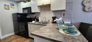 Kitchen featuring white cabinets, a sink, light wood-type flooring, black appliances, and backsplash