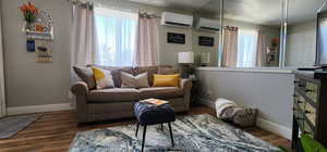 Living room with dark wood-style floors, a wall mounted AC, and baseboards