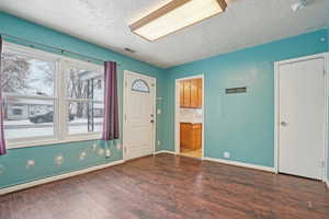 Foyer entrance with dark wood-style floors, visible vents, baseboards, and a textured ceiling