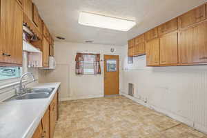 Kitchen with brown cabinetry, light countertops, a sink, and a textured ceiling