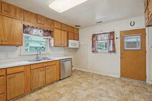 Kitchen featuring light countertops, visible vents, stainless steel dishwasher, white microwave, and a sink