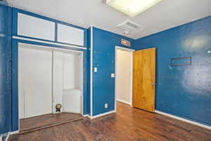 Unfurnished bedroom with dark wood-style floors, baseboards, visible vents, and a textured ceiling