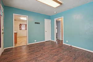 Unfurnished bedroom featuring dark wood finished floors, a textured ceiling, baseboards, and ensuite bath